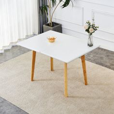 a white table sitting on top of a rug next to a vase filled with flowers