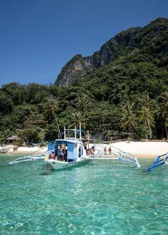 a boat that is floating in the water near some trees and sand with people on it