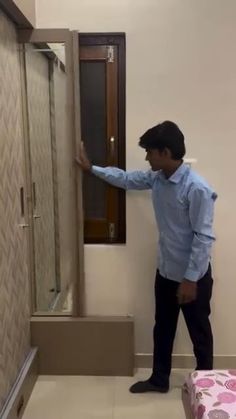 a man standing next to a shower in a room with white walls and tile flooring