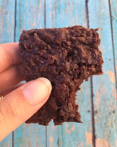 a hand holding a chocolate cookie on top of a blue wooden table next to a piece of wood