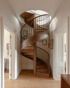 there is a spiral staircase in the middle of this room with wood floors and white walls