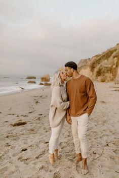 a man and woman standing on top of a sandy beach