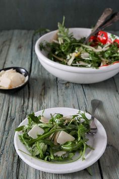 two white bowls filled with salad on top of a wooden table