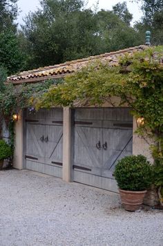 two wooden garages with plants growing on the roof and doors open in front of them