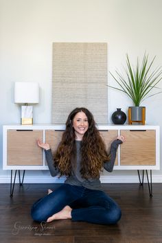 a woman sitting on the floor with her arms wide open in front of an entertainment center