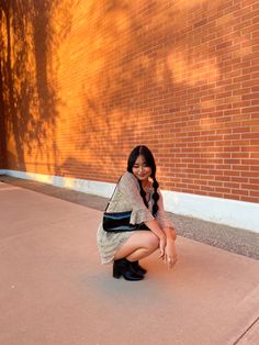 a woman sitting on the ground in front of a brick wall with her legs crossed