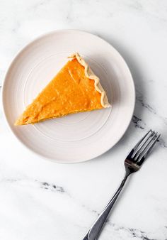 a piece of pie on a white plate next to a silver fork and marble counter top