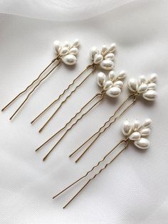 five pairs of hair pins with white flowers on top of each other, sitting on a white cloth