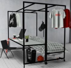 a room with a bed, desk and clothes hanging on the wall next to it