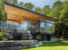 a modern house in the woods surrounded by rocks and grass, with large windows on each side