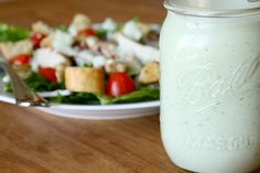 a mason jar filled with salad dressing next to a plate of salad on a table