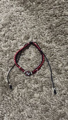 a red and black string bracelet laying on top of a gray carpet next to a cell phone