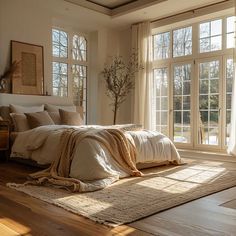 a large bed sitting next to two windows on top of a hard wood floor covered in blankets