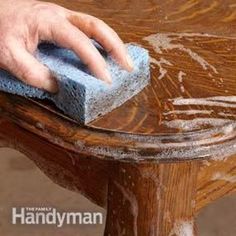 a hand with a sponge on top of a wooden bench that has been stained brown