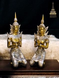 two gold and silver statues sitting on top of a wooden table next to a white rug