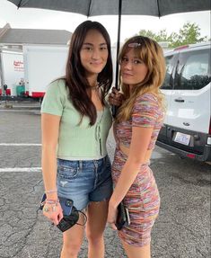 two women standing under an umbrella in a parking lot