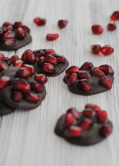 chocolate covered cookies with pomegranates scattered around them on a wooden surface