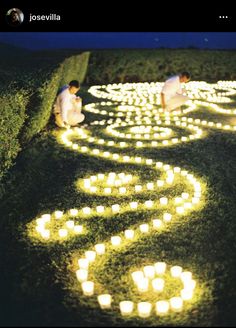 two people sitting on the ground with candles in the shape of a spiral around them