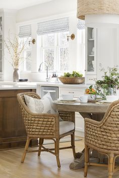 two wicker chairs sit at a round table in the middle of a white kitchen