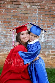 two girls in graduation gowns hugging each other on the grass with brick wall behind them