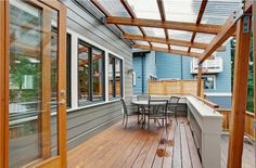 a wooden deck with table and chairs under a pergolated roof over an outdoor dining area