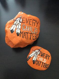 two rocks that say every child matters and each one has an orange rock with feathers on it