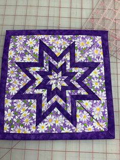 a purple and white quilted piece with flowers on it next to a measuring ruler