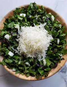 a wooden bowl filled with shredded cheese and greens on top of a marble countertop