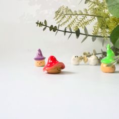 three small toy gnomes sitting next to each other on a white surface with plants in the background