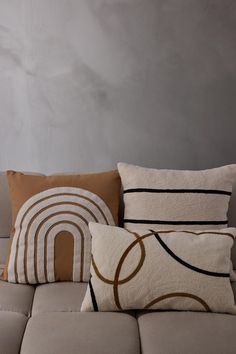 three pillows sitting on top of a couch in front of a gray wall with a brown and white design