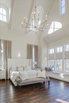 a large white bed sitting inside of a bedroom next to two windows and a chandelier