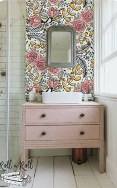 a white sink sitting under a bathroom mirror next to a pink dresser and shower stall