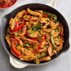 chicken and peppers in a skillet with sauce on the side