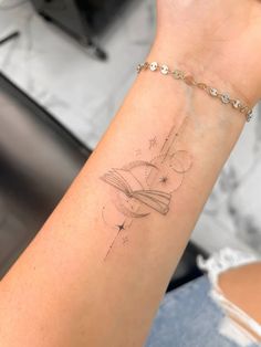 a woman's arm with a book and stars tattoo on her left wrist,