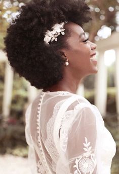 a woman with an afro is smiling and wearing a white dress in front of a tree