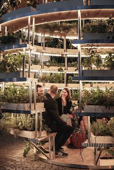 two men and a woman are talking in front of a planter filled with plants