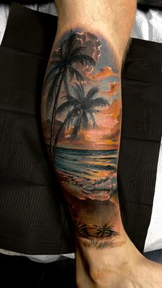 a man's leg with a sunset and palm tree tattoo on his left calf