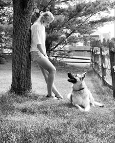 black and white photograph of a woman sitting next to a dog on the grass near a tree