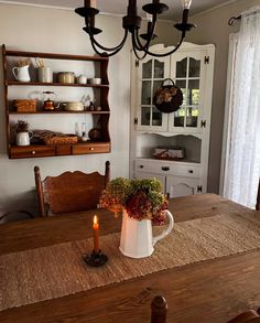 a dining room table with a white pitcher on it and a candle in the center