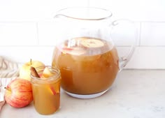 two pitchers of apple cider next to some apples