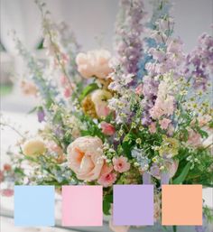 a vase filled with lots of flowers on top of a white table covered in pastel colors