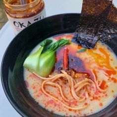 a black bowl filled with soup and vegetables on top of a white table next to a bottle