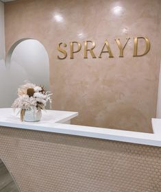 a vase with flowers sitting on top of a counter in front of a sign that says spray d