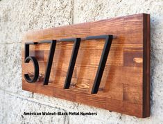 a wooden house number sign mounted to the side of a building with metal numbers on it