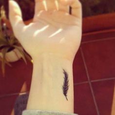 a person's hand with a small feather tattoo on it