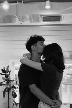 black and white photograph of two people kissing each other in front of a potted plant