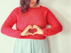 a woman in a red sweater is holding her hands together and making a heart shape