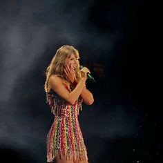 a woman in a colorful dress holding a microphone up to her face while standing on stage