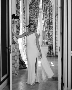 a woman in a white dress is walking into a room with curtains and drapes