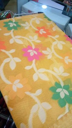 an orange table cloth with pink and green flowers on it, sitting on a metal rack